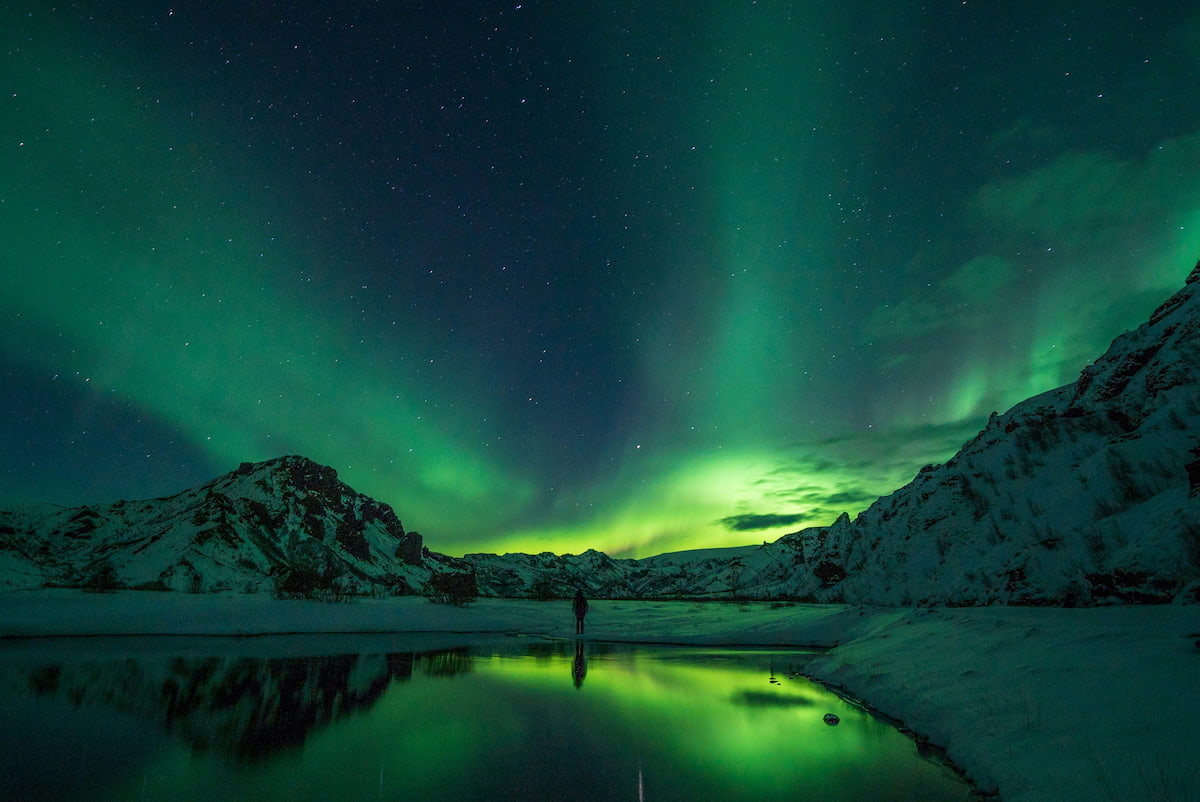 Vibrant green and purple aurora borealis over snow-covered mountains.