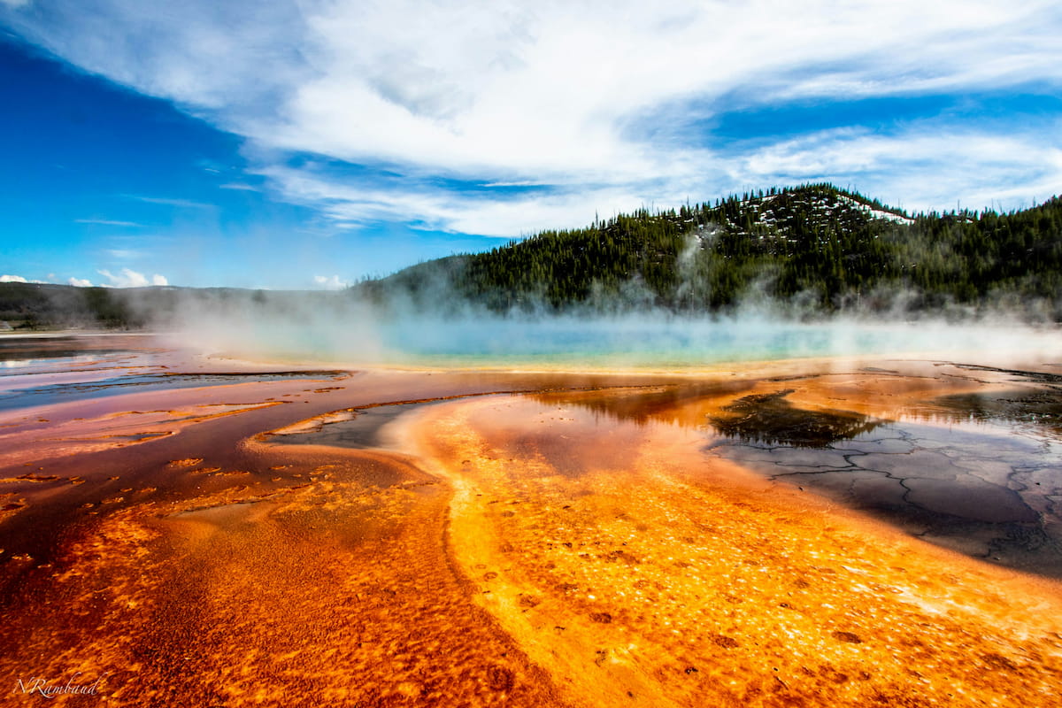 Eruption of Old Faithful geyser with steam rising against a blue sky.